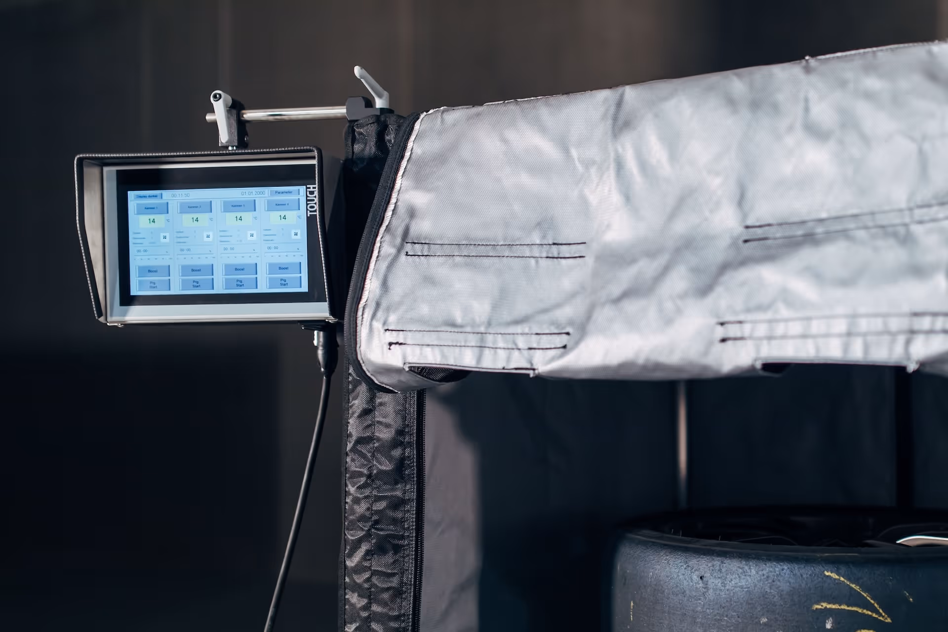 Close-up of a touchscreen control panel with settings displayed, attached to a piece of industrial equipment covered in a gray protective fabric.