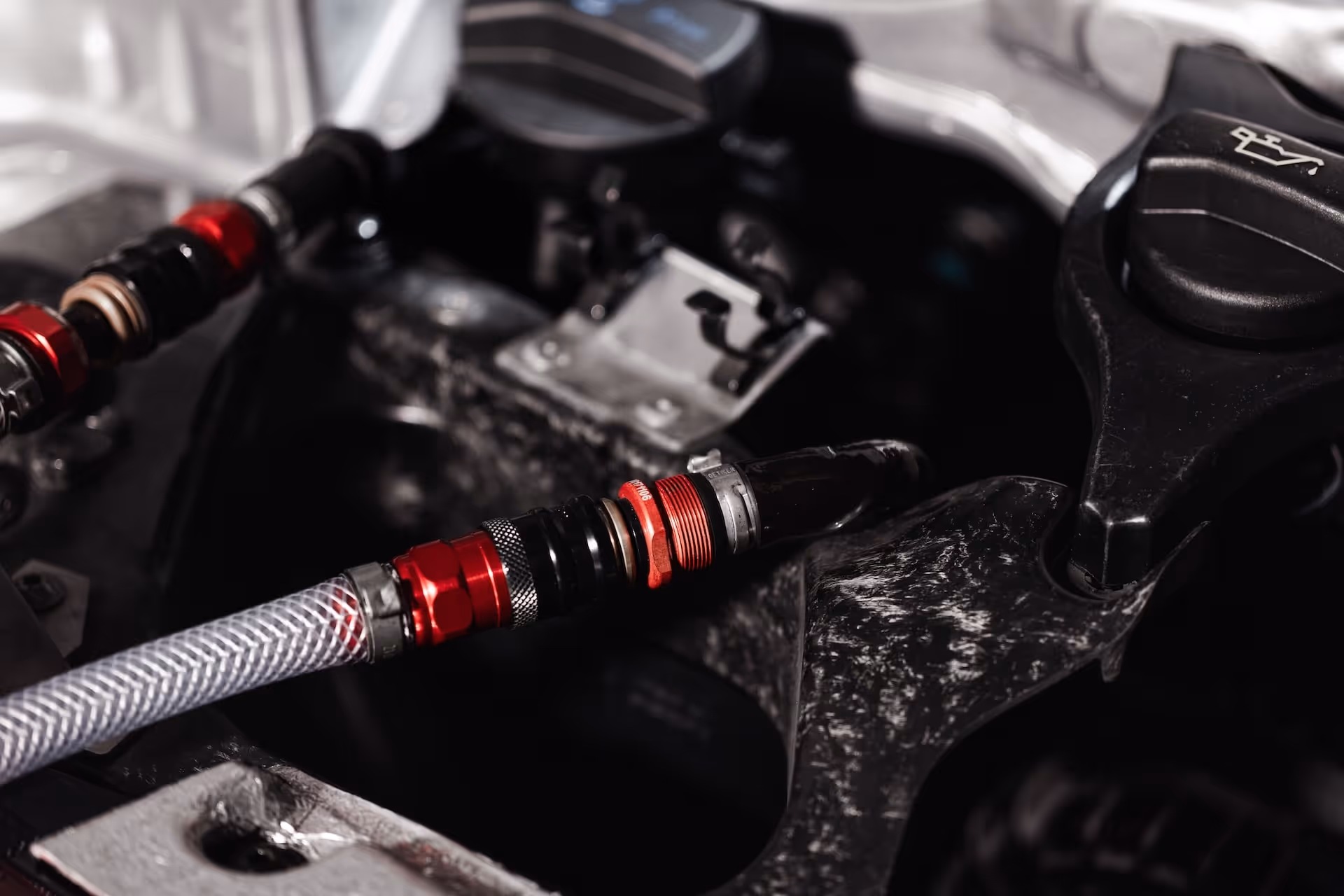 Close-up of a car engine oil filler cap and a braided hose with red connectors inside the engine compartment.