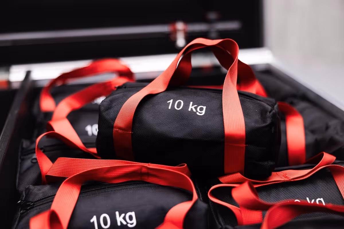 Black weight bags with red handles labeled '10 kg' stacked inside a black carrying case.