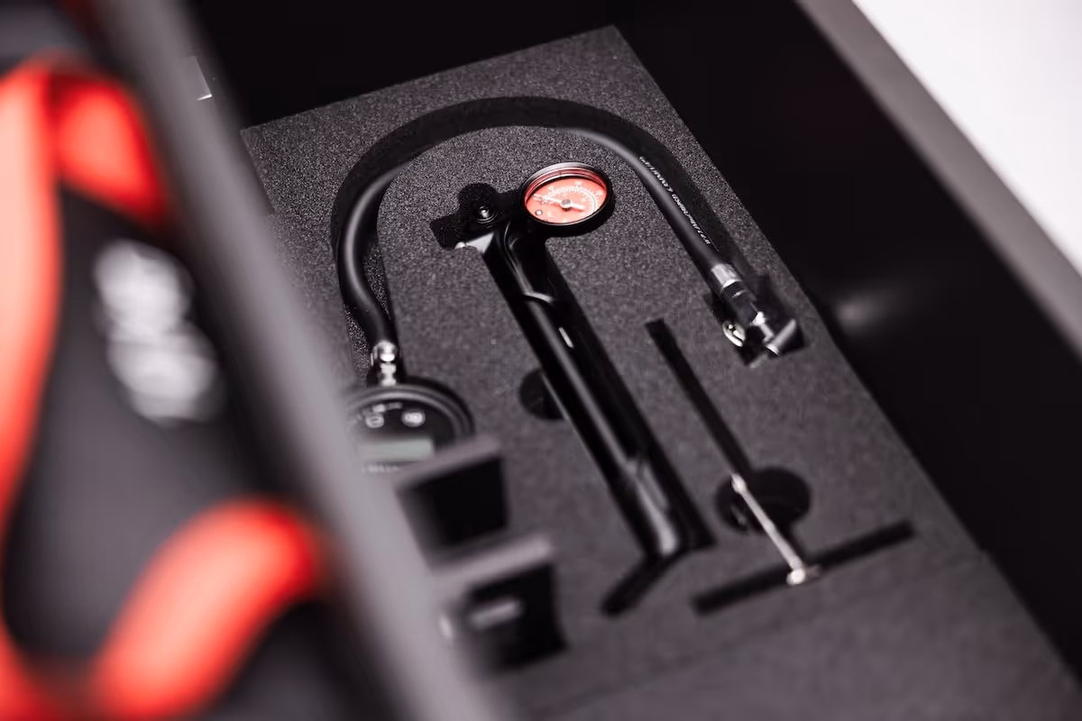 Close-up of a black tire pressure gauge with a red dial, housed in a foam insert inside a box.