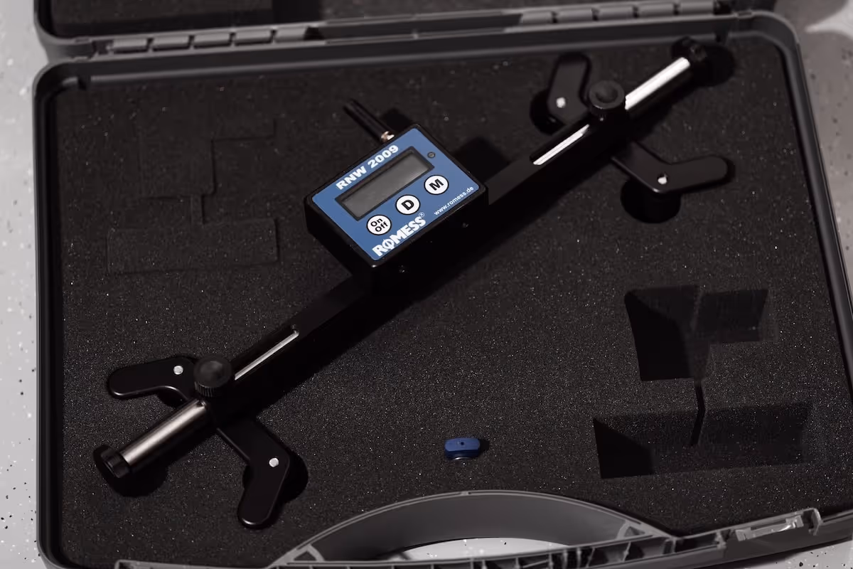 Digital measuring instrument with a blue display unit labeled RNW 2009 placed inside a black foam-lined carrying case.