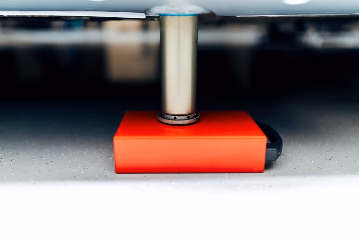Close-up of a metal air lift leg resting on a red rectangular block on a speckled workshop floor.