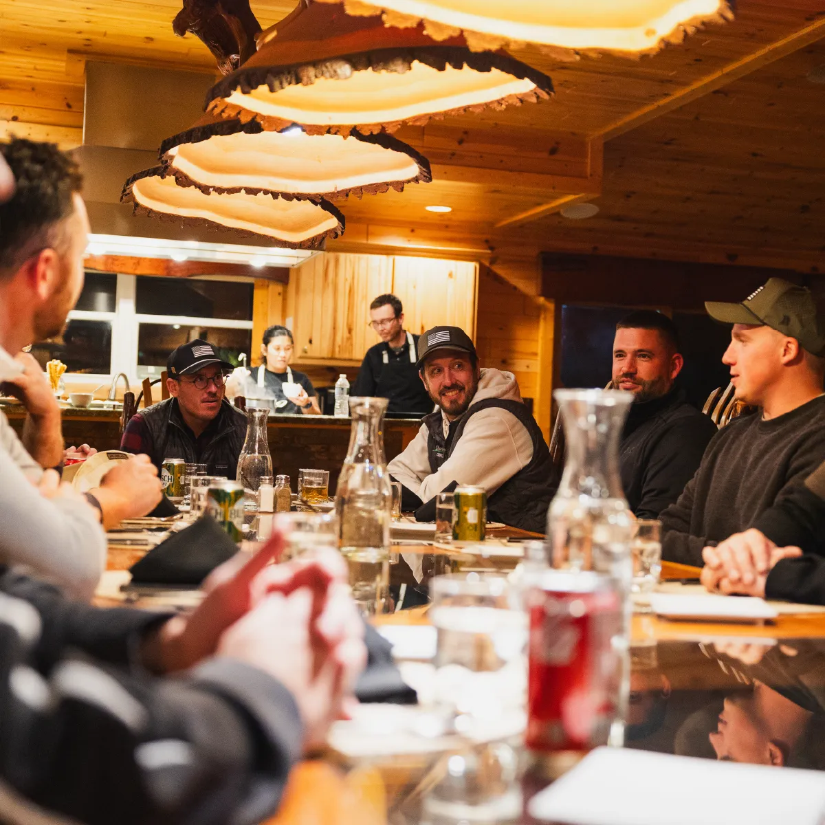 Group of men sitting around a wooden table in a warmly lit room with rustic decor, smiling and engaging in conversation.