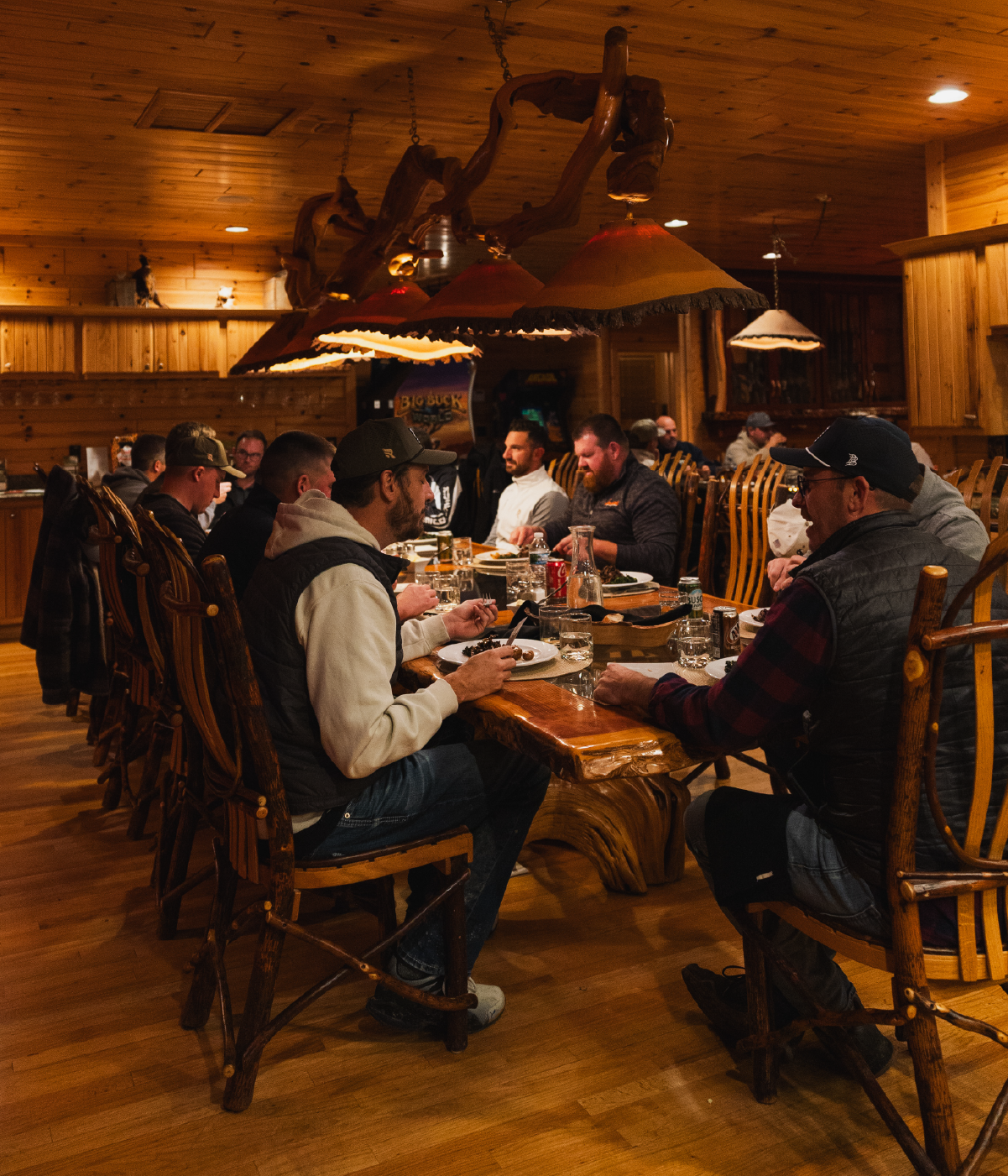 Group of men sitting around a rustic wooden table enjoying a meal in a cozy, wood-paneled room with warm lighting.