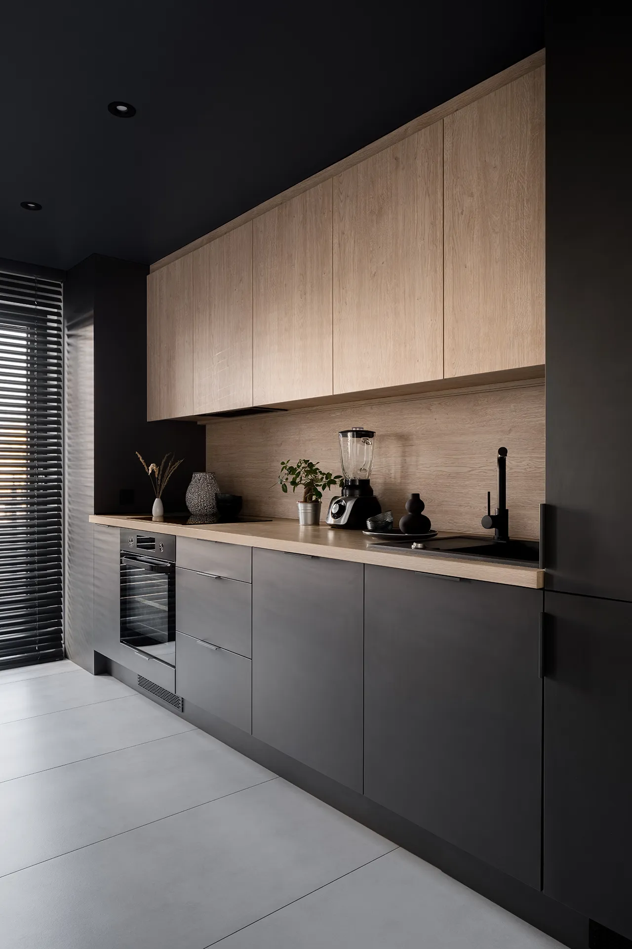 Moderne Küche mit schwarzen Unterschränken, hellen Oberschränken aus Holz, Holzarbeitsplatte, Backofen, Mixer, Pflanzen und schwarzem Wasserhahn.