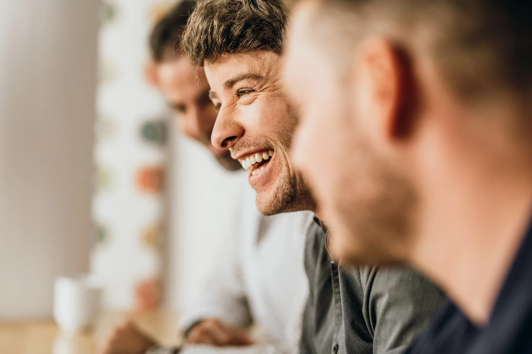 Drei Männer sitzen nah beieinander und lachen gemeinsam.