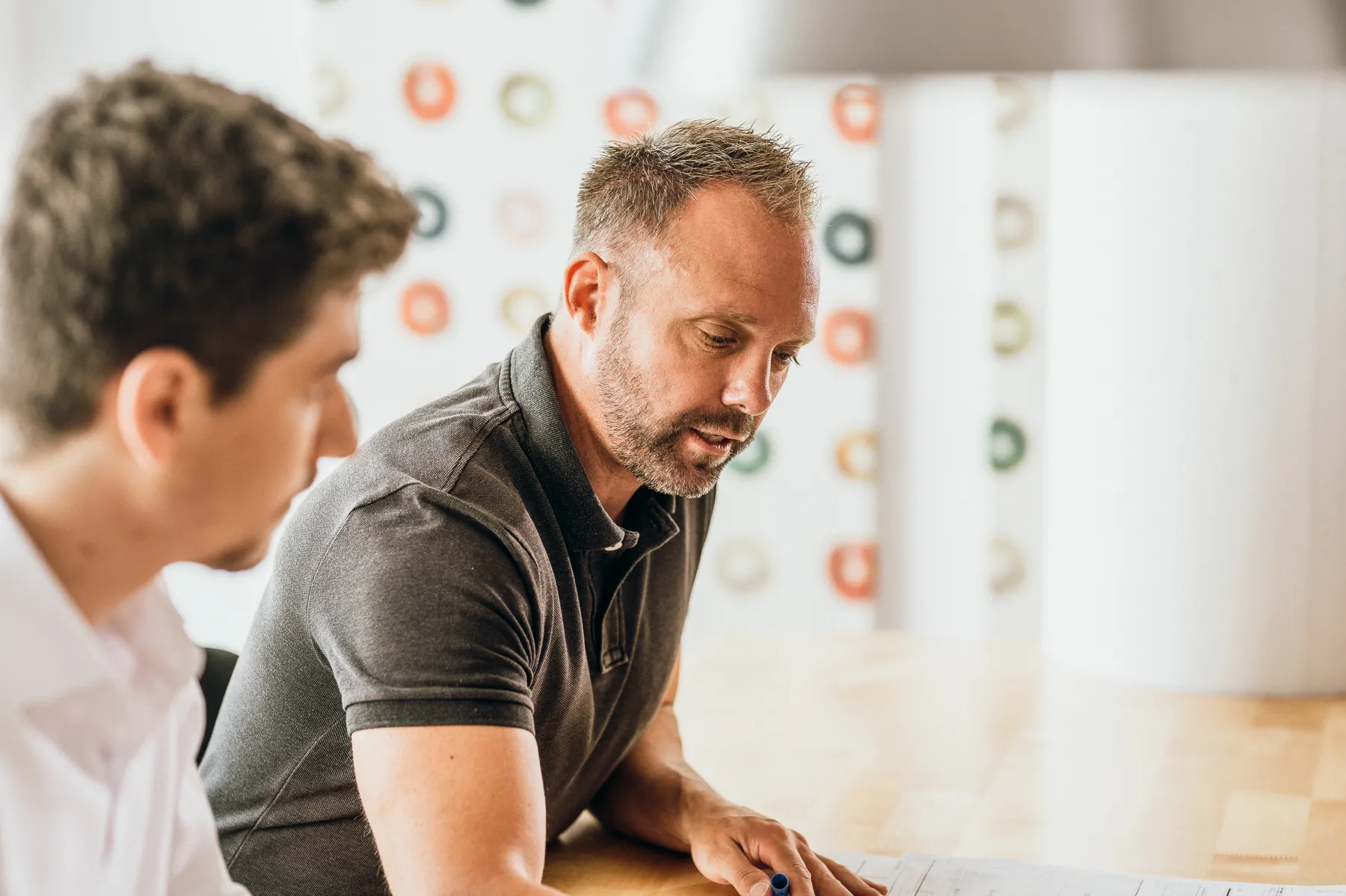 Zwei Männer sitzen an einem Tisch und besprechen Pläne oder Dokumente.