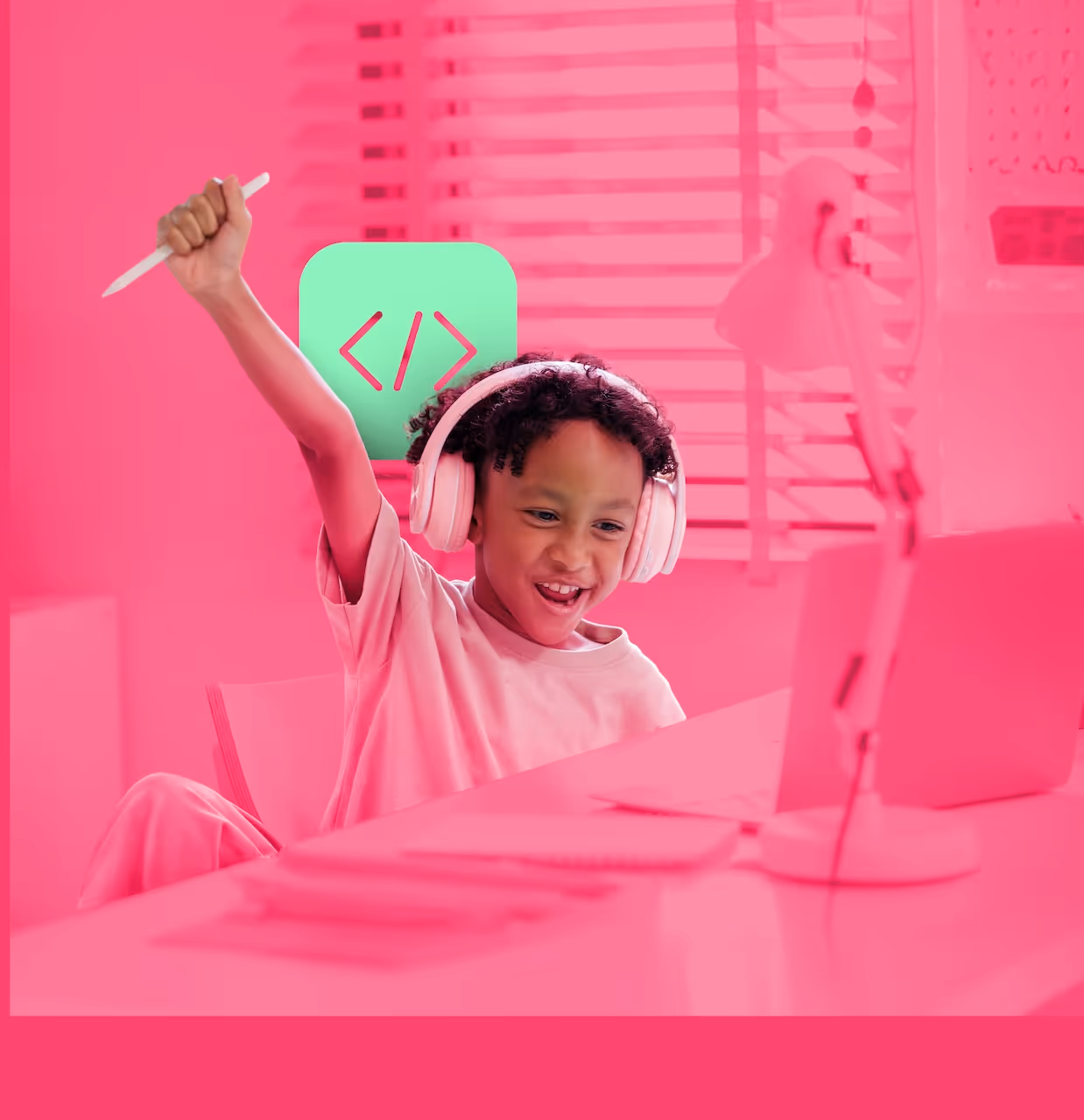 Niño emocionado con audífonos levantando la mano mientras usa una computadora portátil en un escritorio.