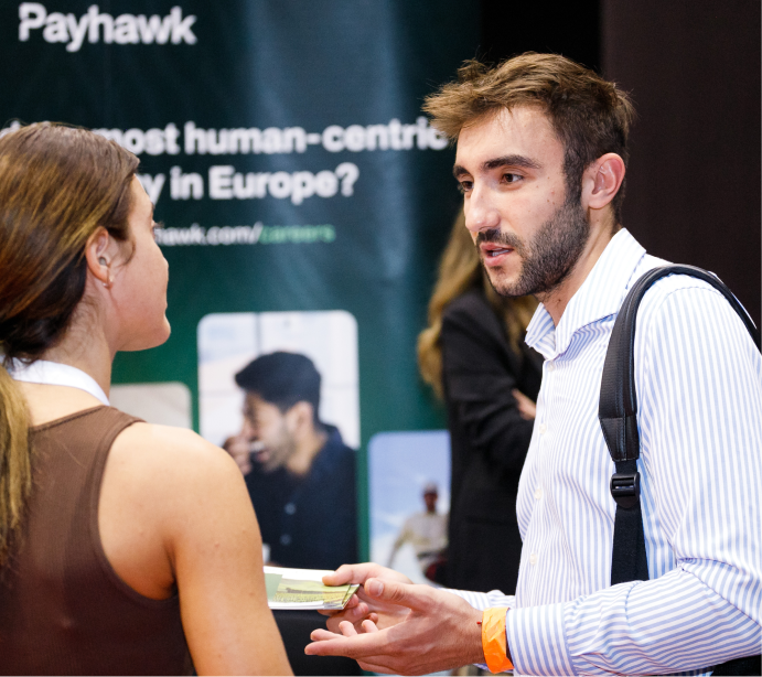 Medium shot photograph of two individuals talking, with a sign in background.