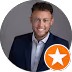 Smiling man in a dark blazer and white shirt against a gray background with an orange star badge overlay. - Total Quality Lending Images