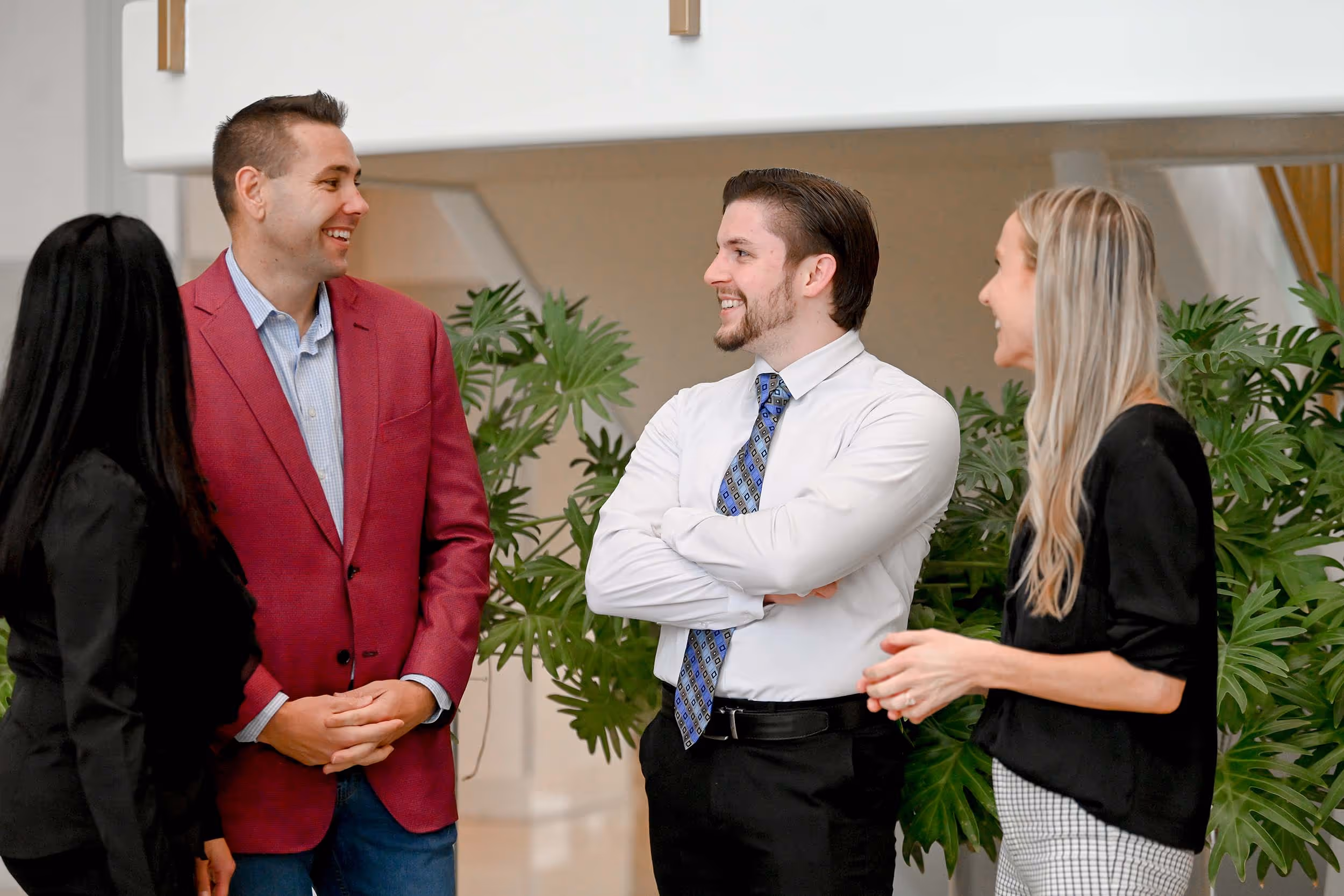 Four colleagues smiling and chatting in an office with green plants in the background. - Total Quality Lending Images