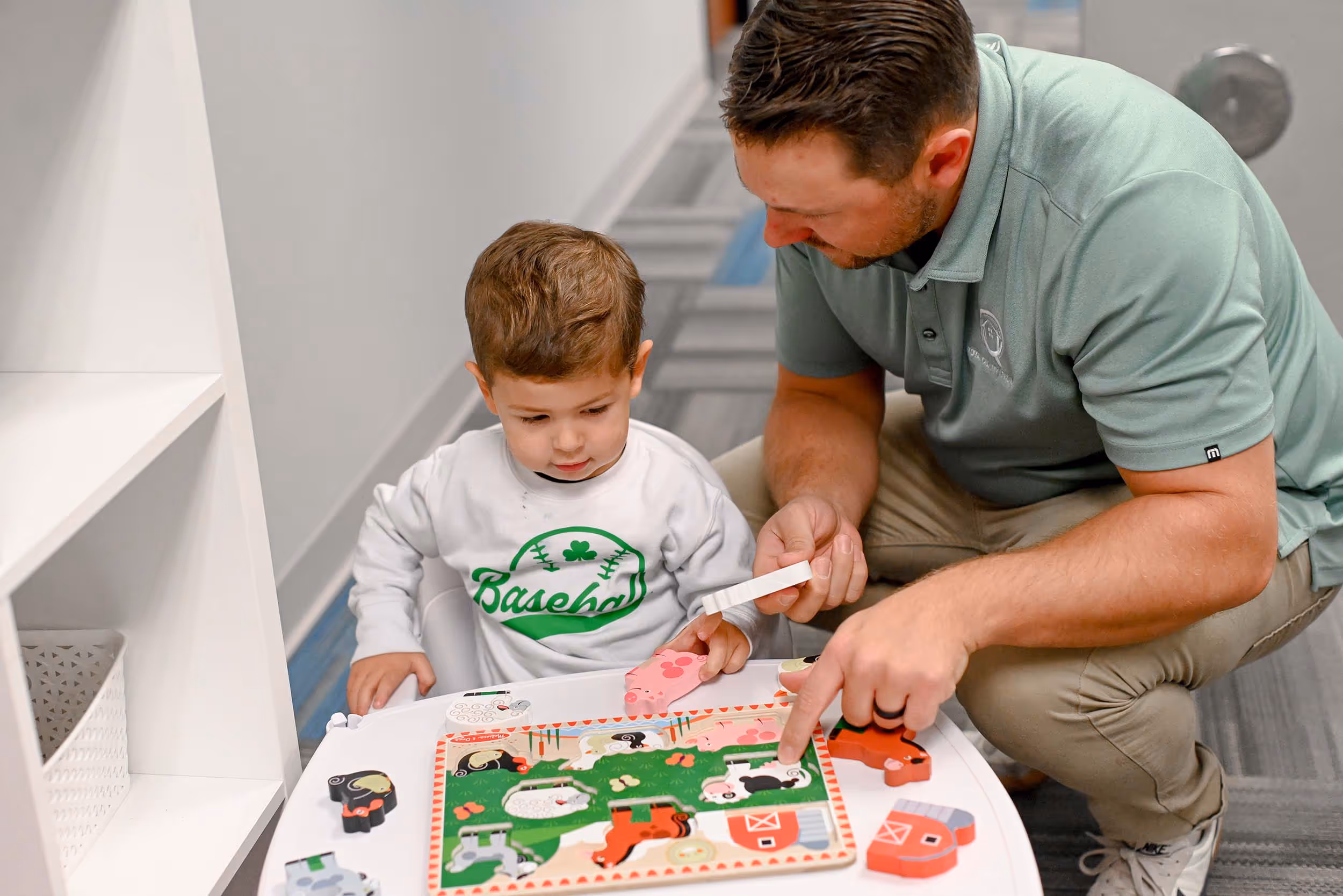 An adult man and a young boy solving a wooden farm animal puzzle together at a white table. - Total Quality Lending Images