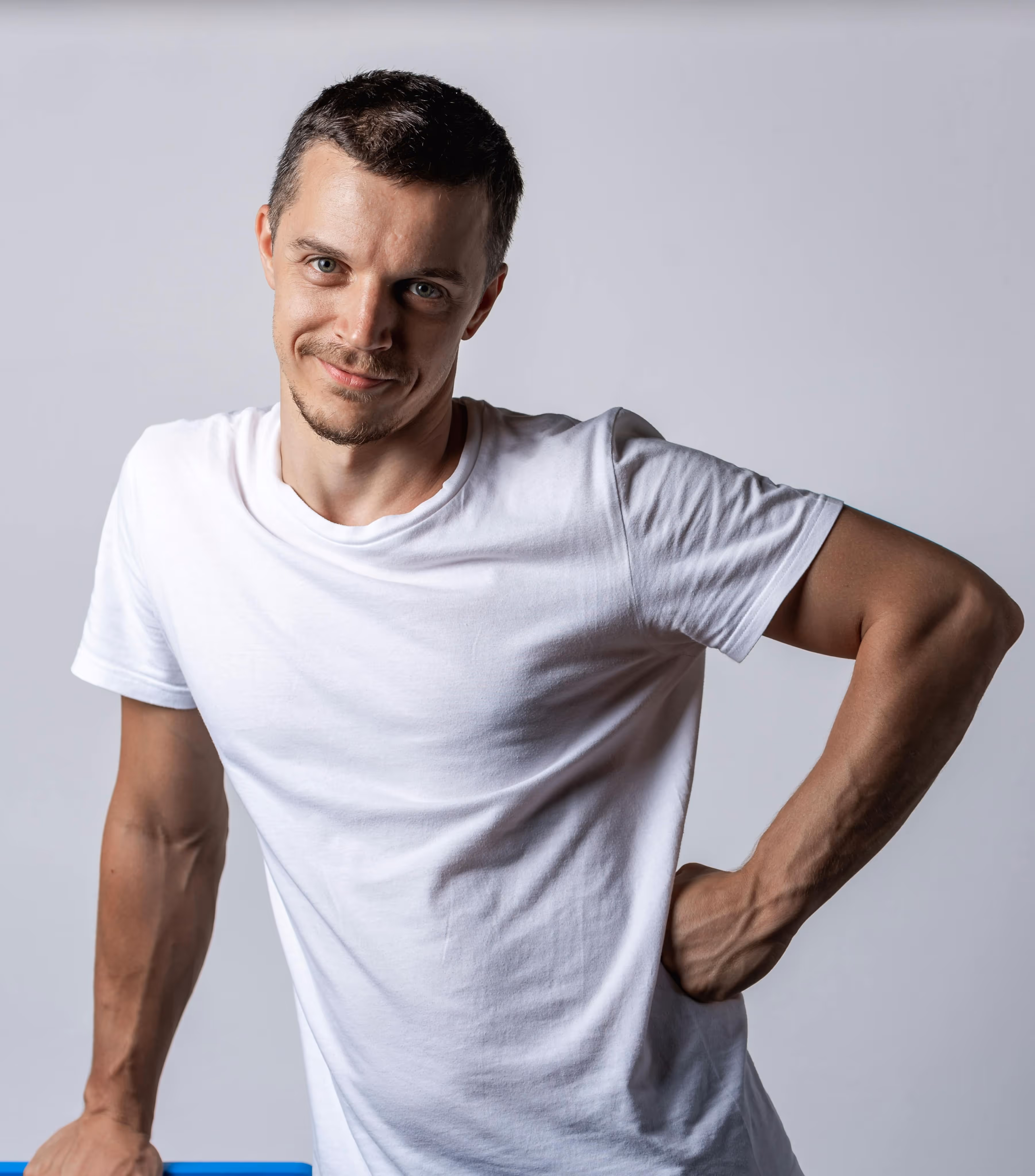 Man in a white t-shirt smiling and leaning on a blue surface against a gray background. - Total Quality Lending Images