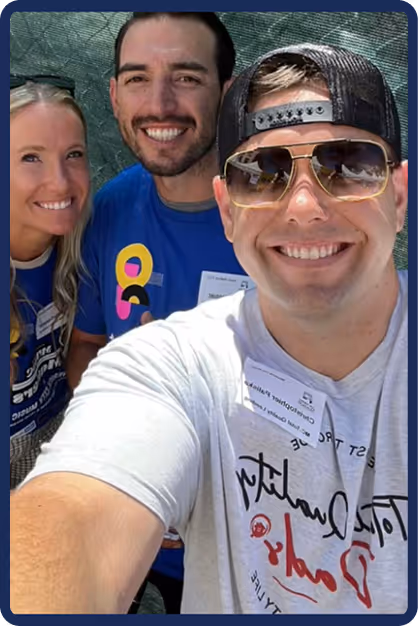 Three smiling adults taking a close-up selfie outdoors, with one wearing sunglasses and a backward cap. - Total Quality Lending Images