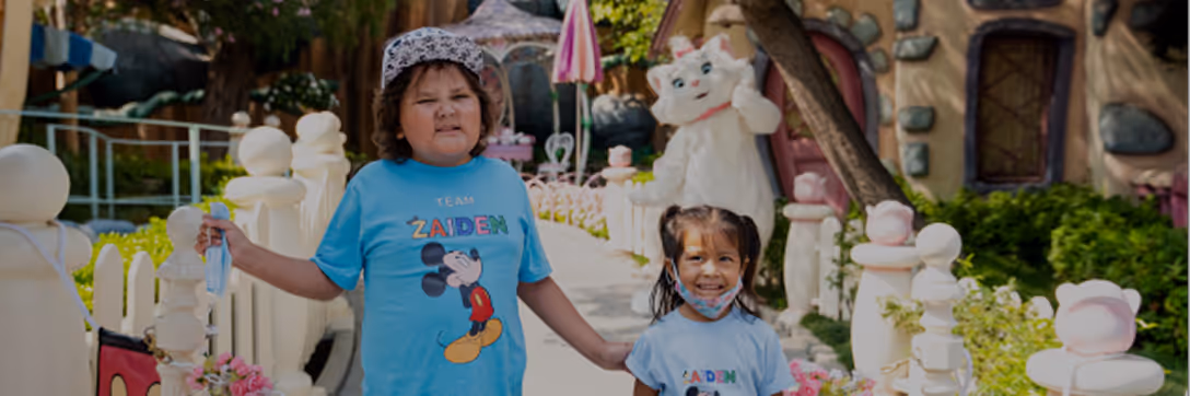 Two children holding hands and smiling, wearing matching blue Mickey Mouse shirts in a themed park setting. - Total Quality Lending Images