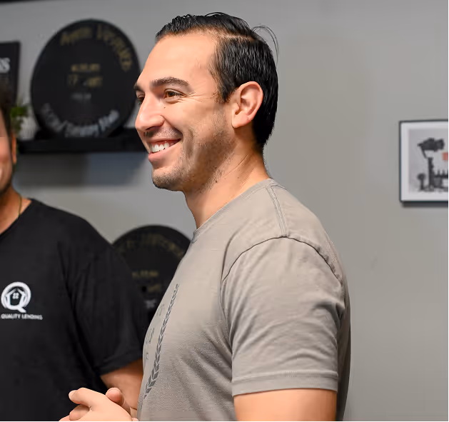 Smiling man with short dark hair wearing a grey t-shirt standing indoors. - Total Quality Lending Images