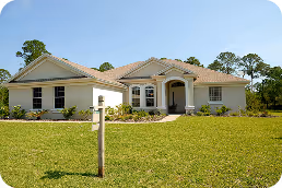 Single-story house with beige exterior, a wide front lawn, and a wooden signpost in the foreground. - Total Quality Lending Images