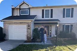Two people standing on the front lawn in front of a two-story house with white siding, stone accents, and a garage. - Total Quality Lending Images