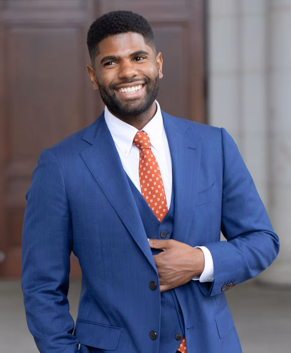 Smiling man in a blue suit with a white shirt and red patterned tie, standing with one hand adjusting his jacket. - Total Quality Lending Images