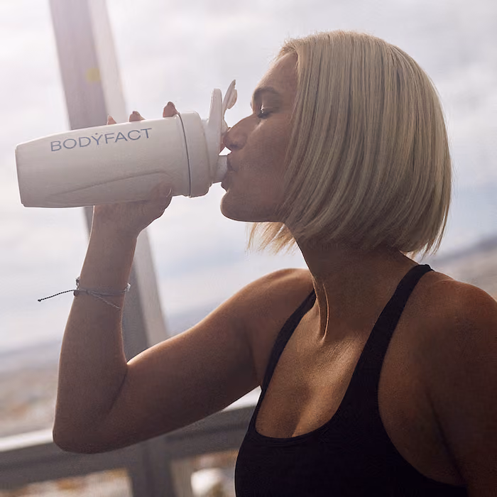 Blonde Frau trinkt aus einer BODYFACT Shaker-Flasche.