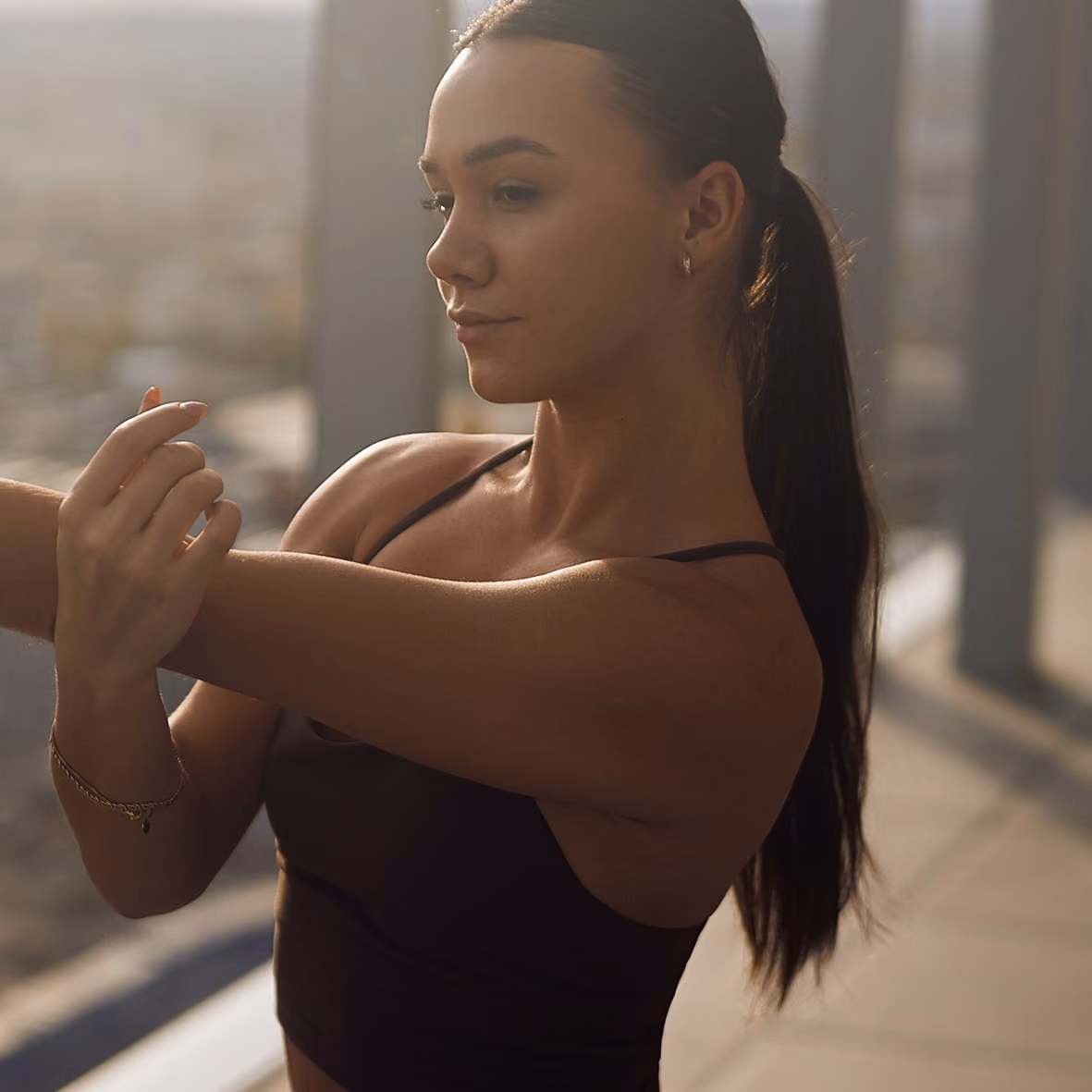 Frau dehnt ihren Arm beim Training auf einer Dachterrasse.