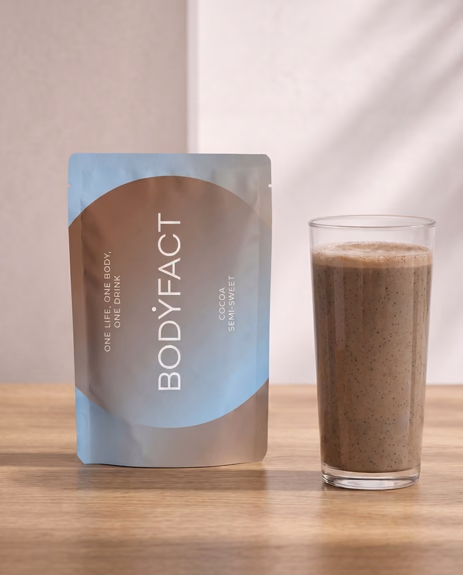 BODYFACT Cocoa Semi-Sweet Beutel neben einem Glas Shake auf einem Holztisch.
