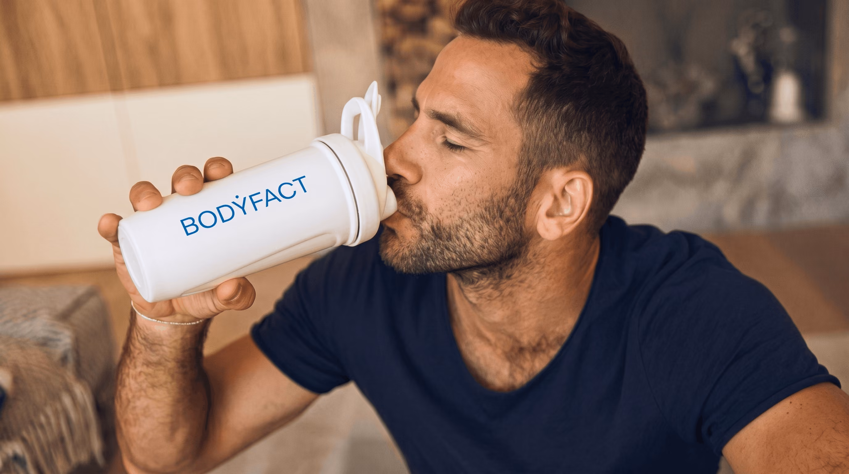 Férfi közelről fehér BODYFACT shakerből iszik, csukott szemmel.