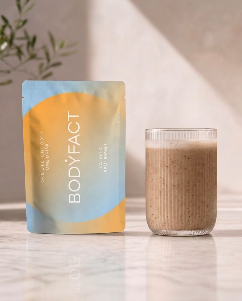 BODYFACT Vanilla Semi-Sweet tasakos ital pohárba töltve, márványpulton, háttérben növénnyel.