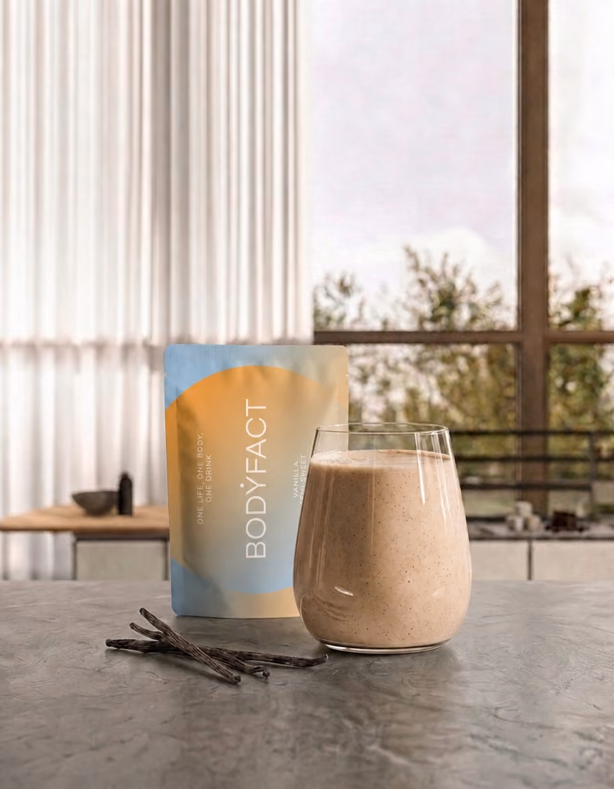 BODYFACT Vanilla Semi-Sweet tasak és egy pohár vaníliás ital, vaníliarudakkal, nagy ablakos belső térben.
