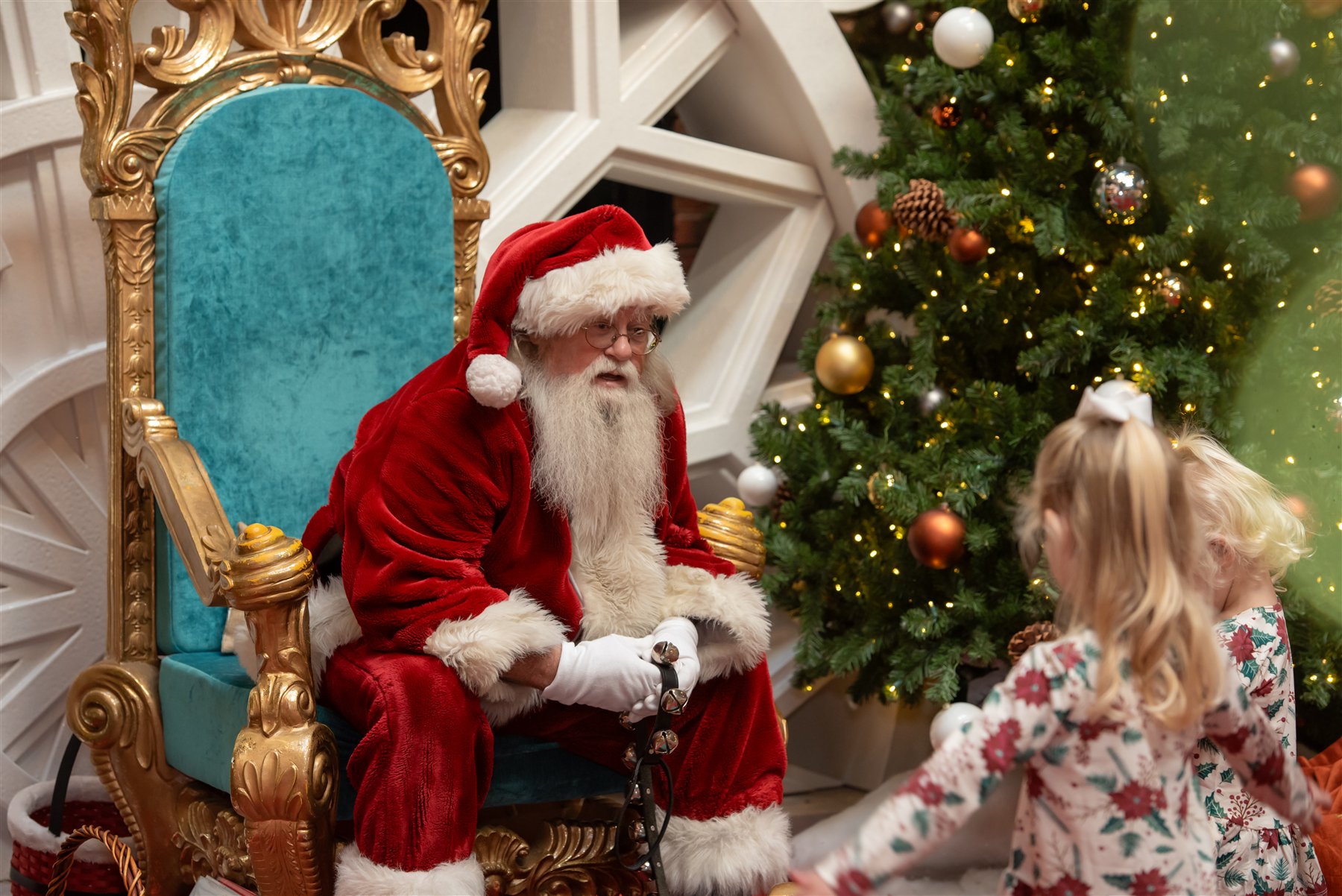 Santa Marty greeting two girls from his gold and turquoise Christmas chair