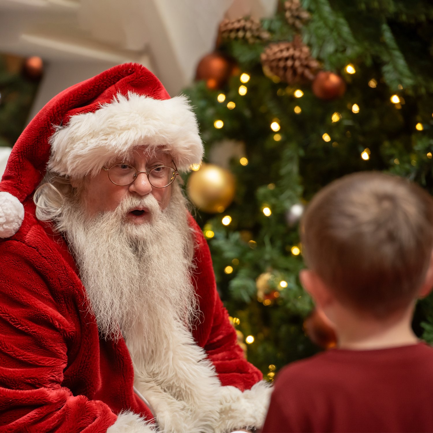Santa Marty sharing a moment of wonder with a boy beside a Christmas tree