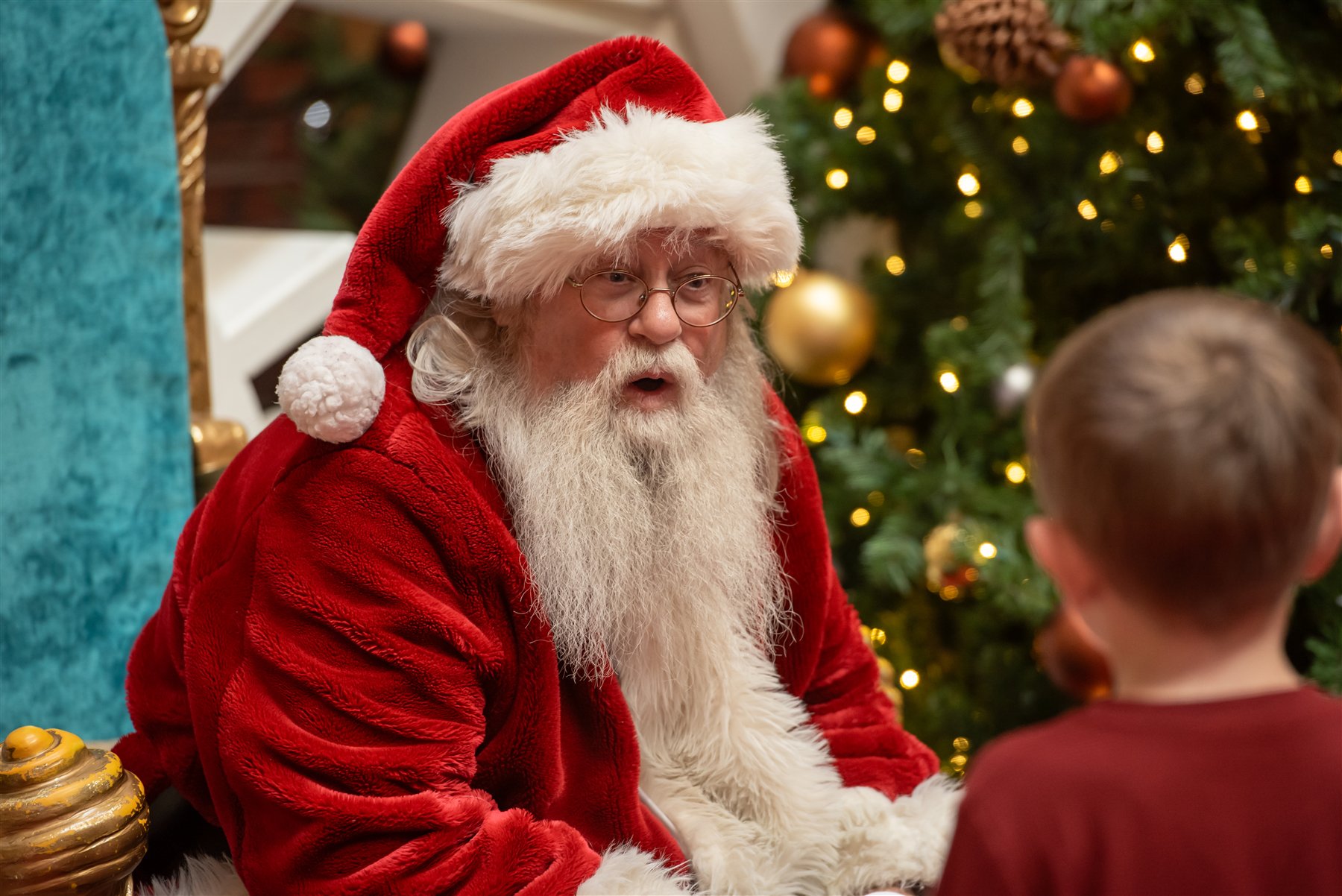 Santa Marty talking with a boy in a burgundy shirt beside a decorated tree