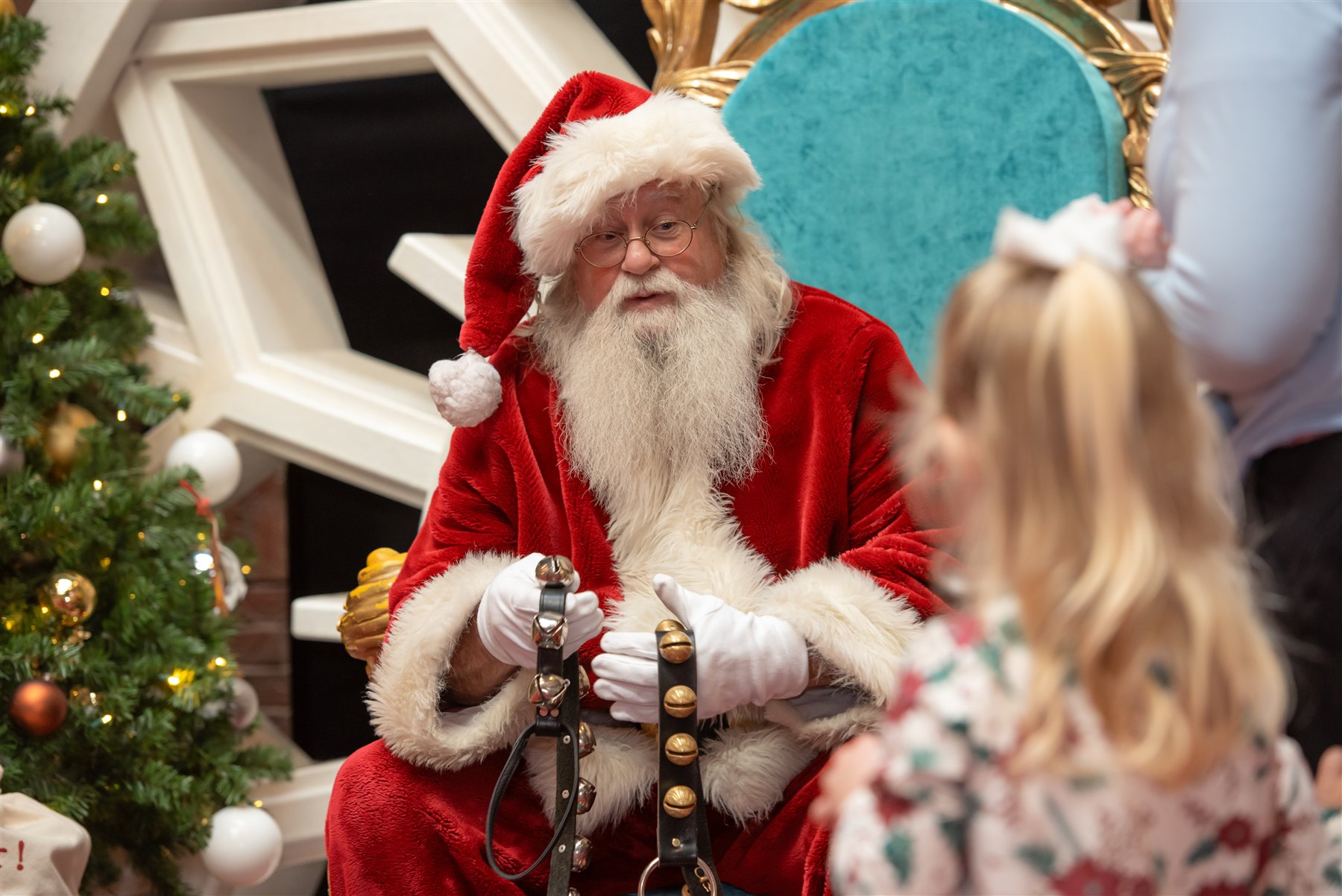 Santa Marty showing sleigh bells to a girl wearing a white hair bow
