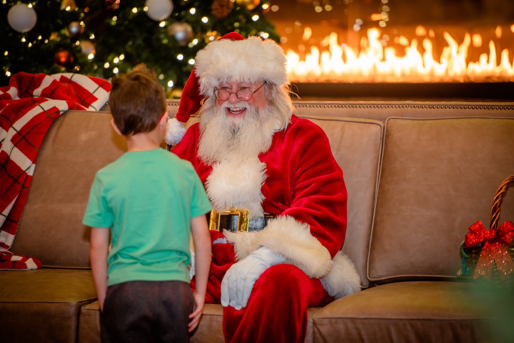 Santa Marty laughing with a boy in a green shirt beside the fireplace