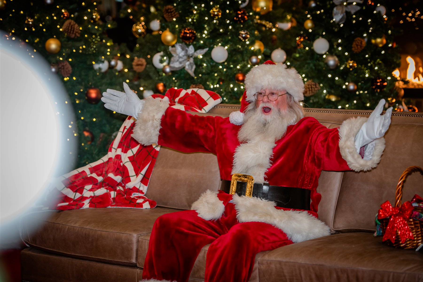 Santa Marty spreading his arms in welcome beside Christmas trees