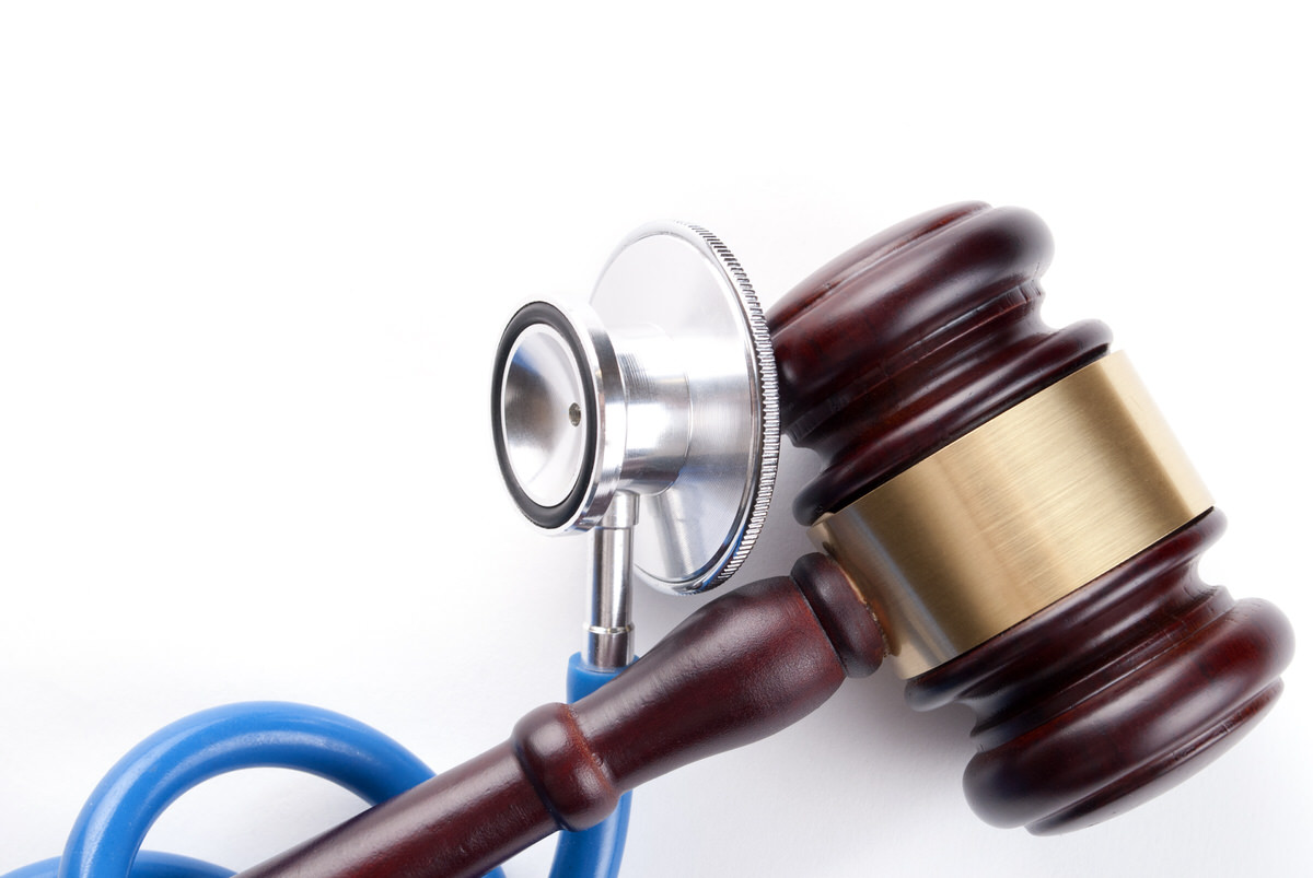 Wooden judge's gavel resting against a stethoscope on a white background.