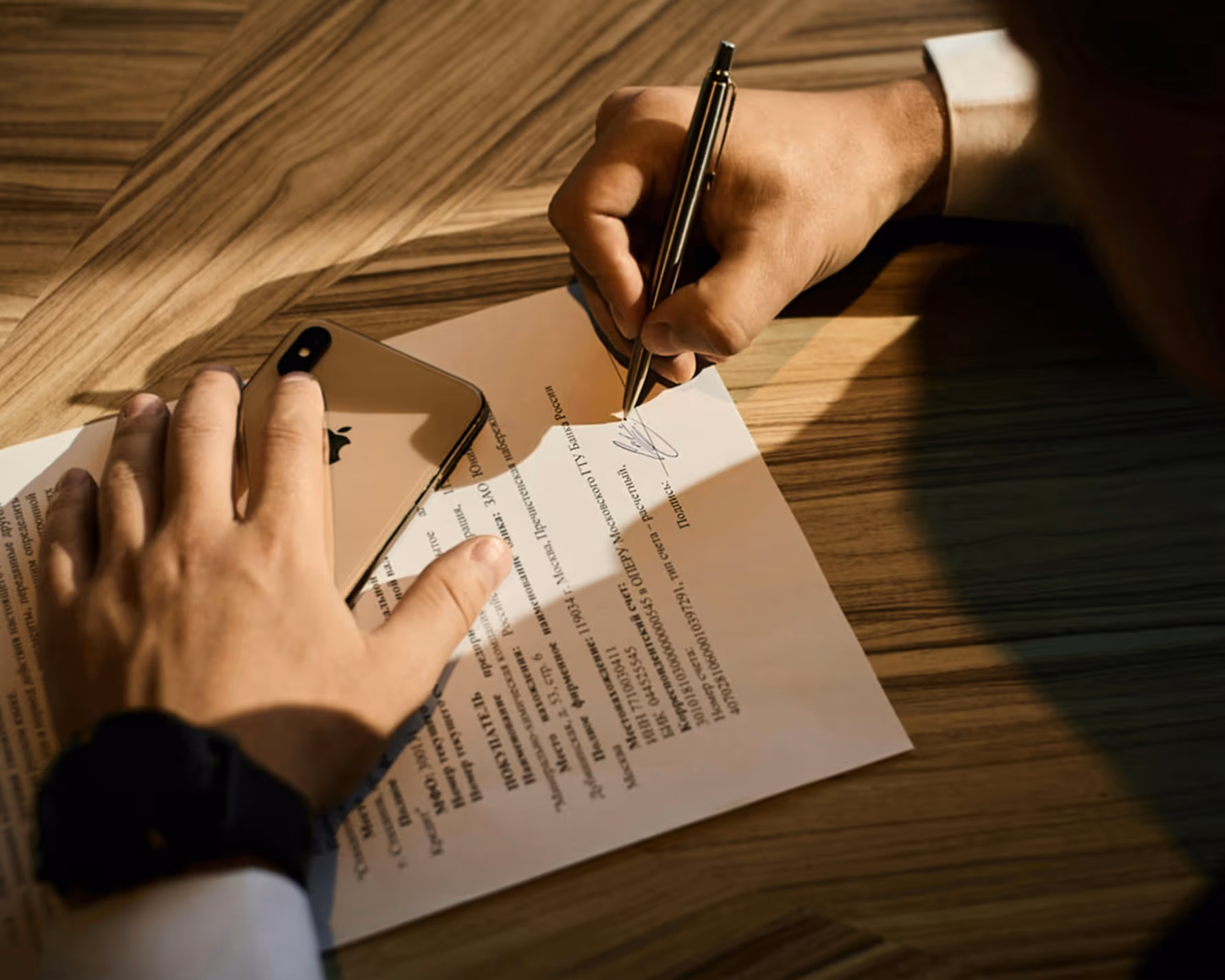 Person signing a document on a wooden table.