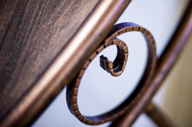 Dettaglio ravvicinato di un pezzo di mobili in legno con una decorazione a spirale in metallo brunito.