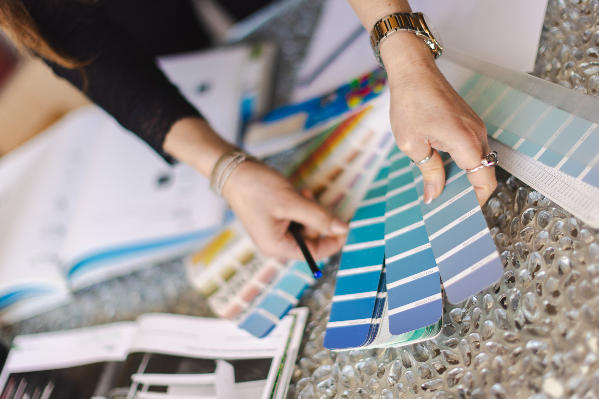 Mani di una persona che sfogliano una tavolozza di colori blu per la scelta della pittura su un tavolo con riviste e materiali di design.