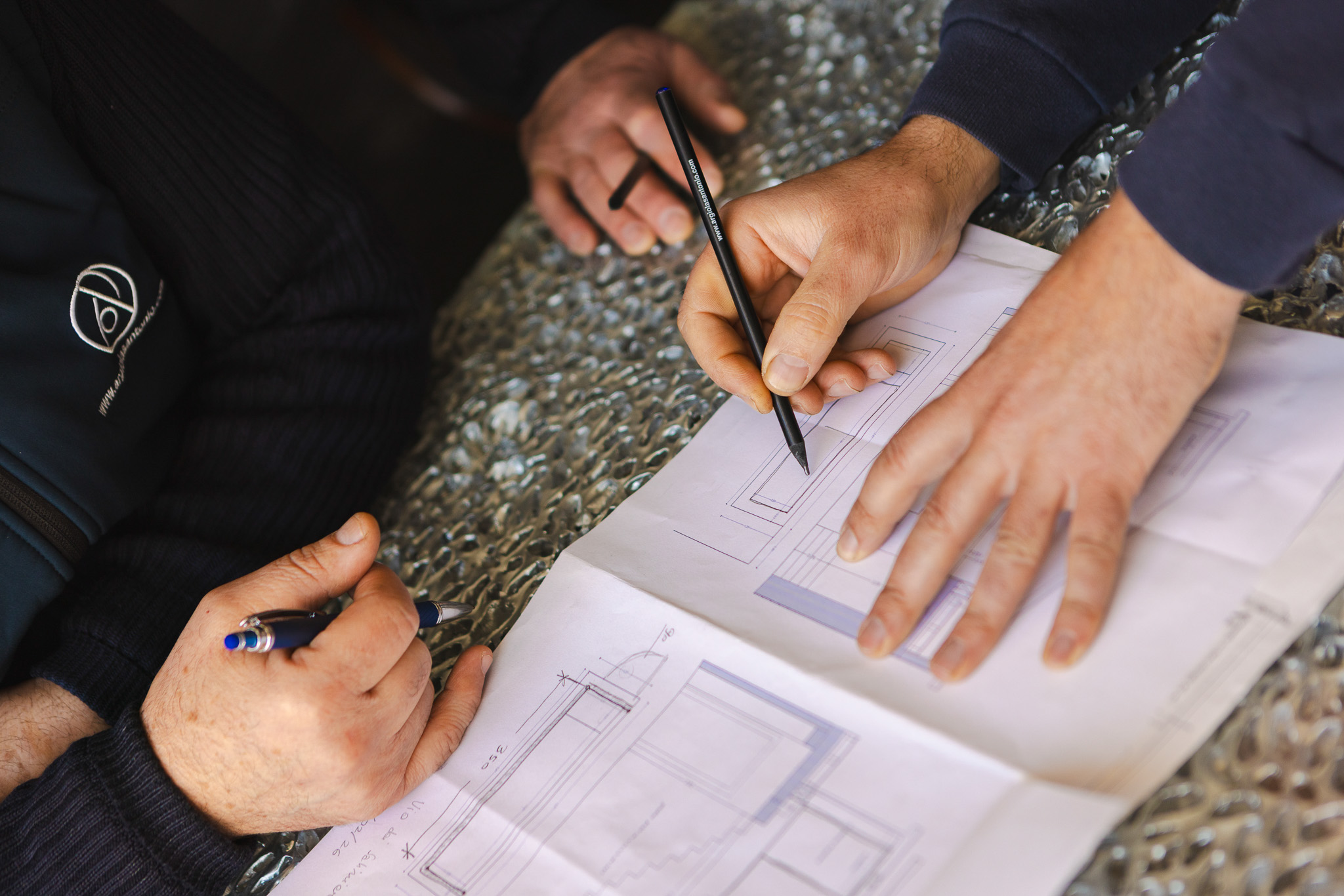 Due mani maschili che progettano e discutono un disegno tecnico su un tavolo con superficie in pellicola a bolle.