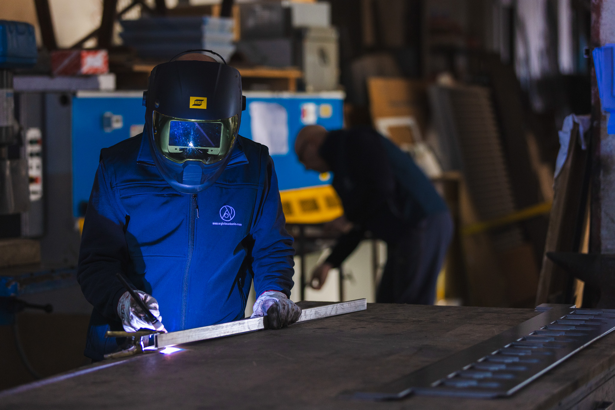 Operaio con casco da saldatore che salda una barra di metallo in un'officina.