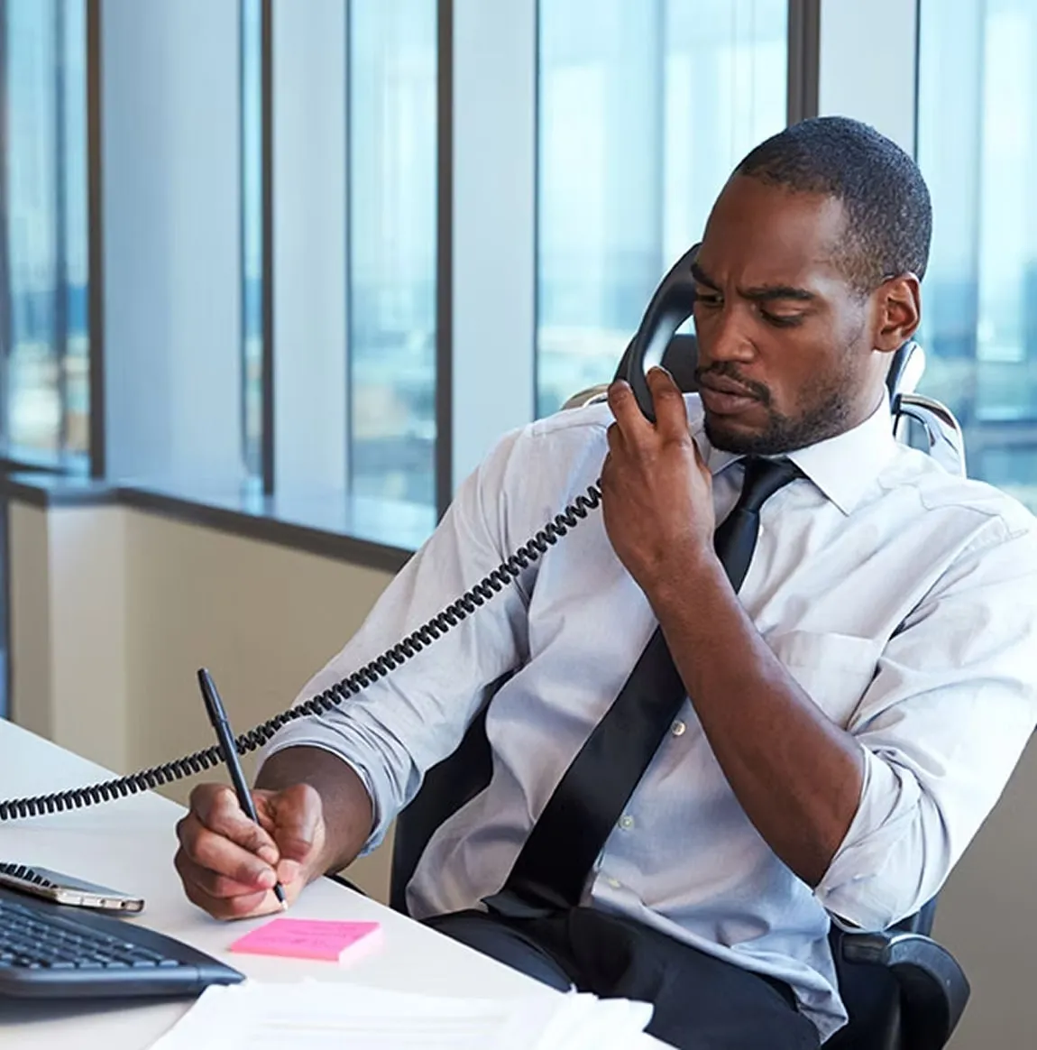Man on a desk phone writing notes in an office