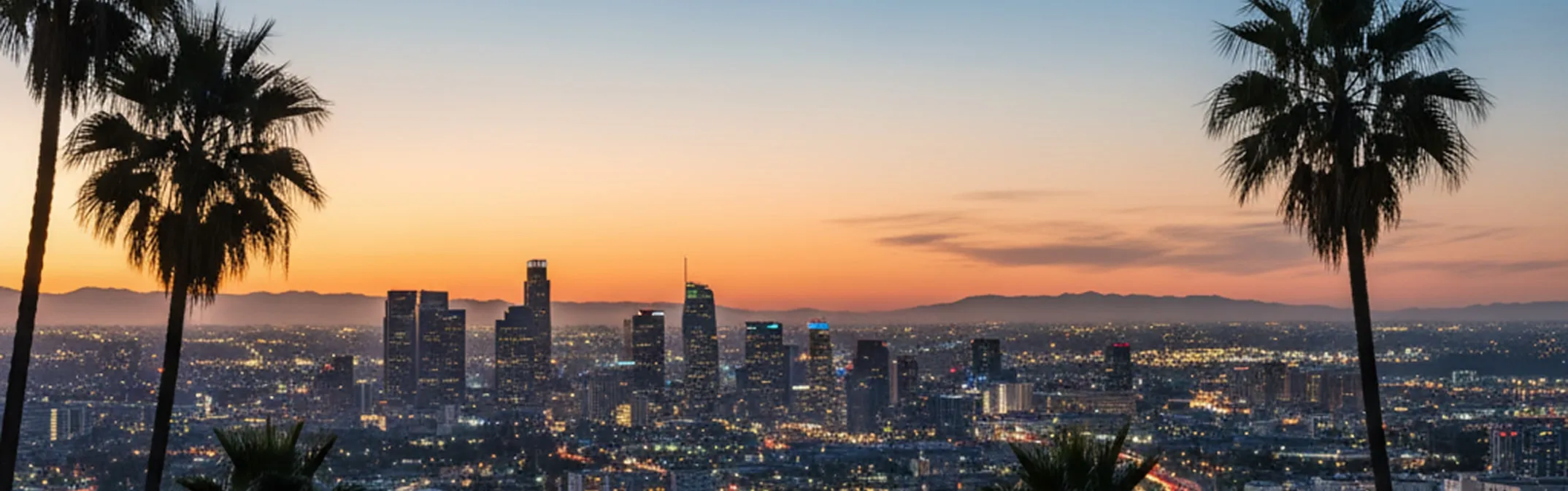 Los Angeles skyline at sunset framed by palm trees