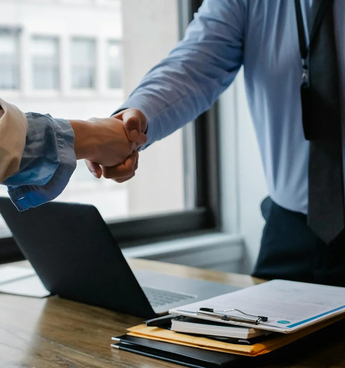 Two people shaking hands over a desk with paperwork