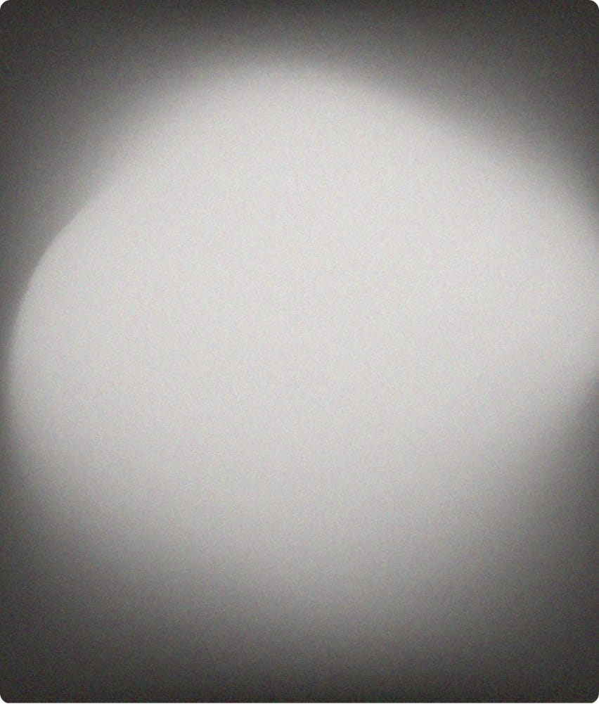 Out-of-focus blurry grayscale image with a bright central spot and dark edges.