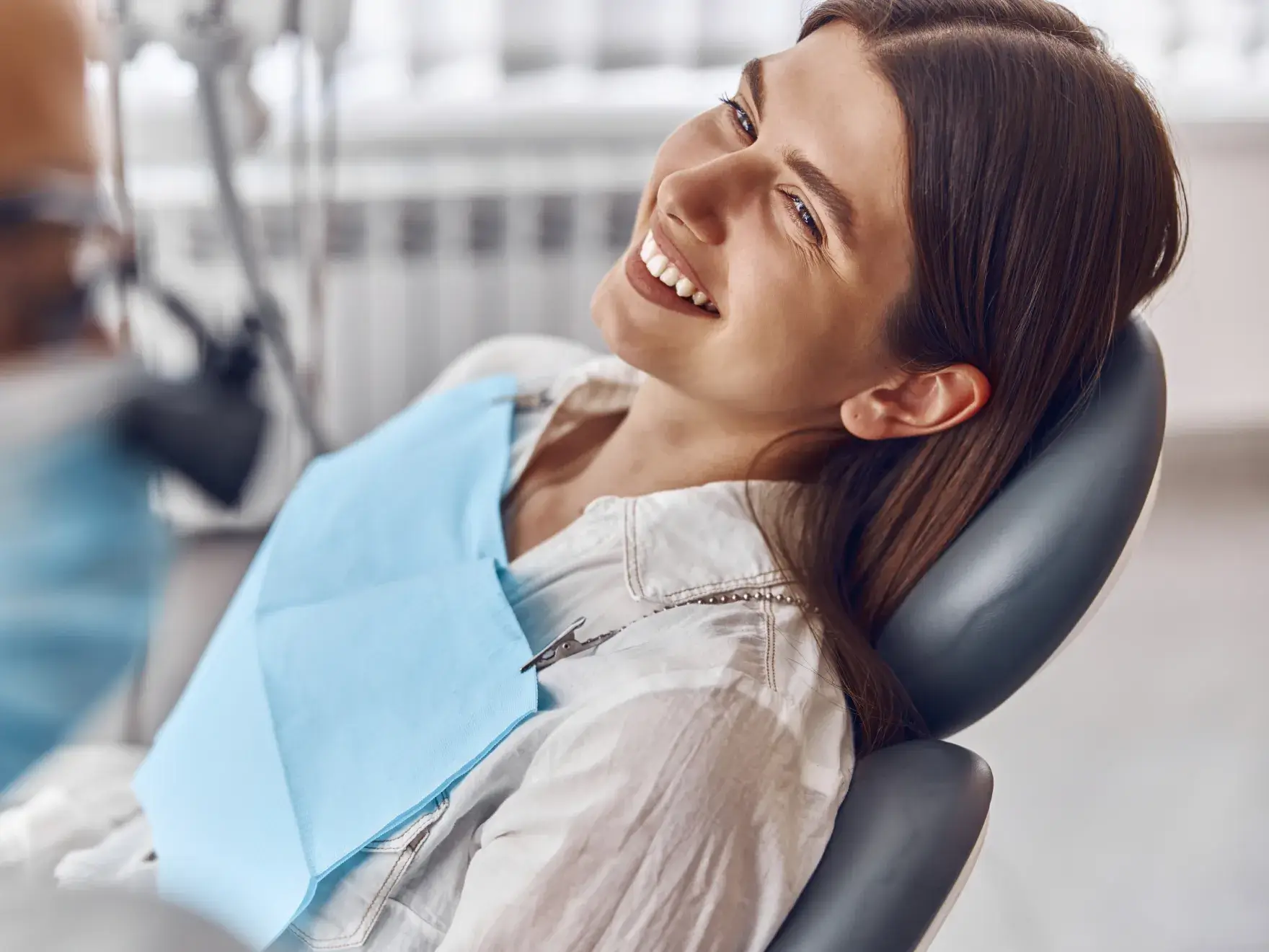 Smiling woman reclining in a dental chair wearing a blue dental bib during a dental visit.