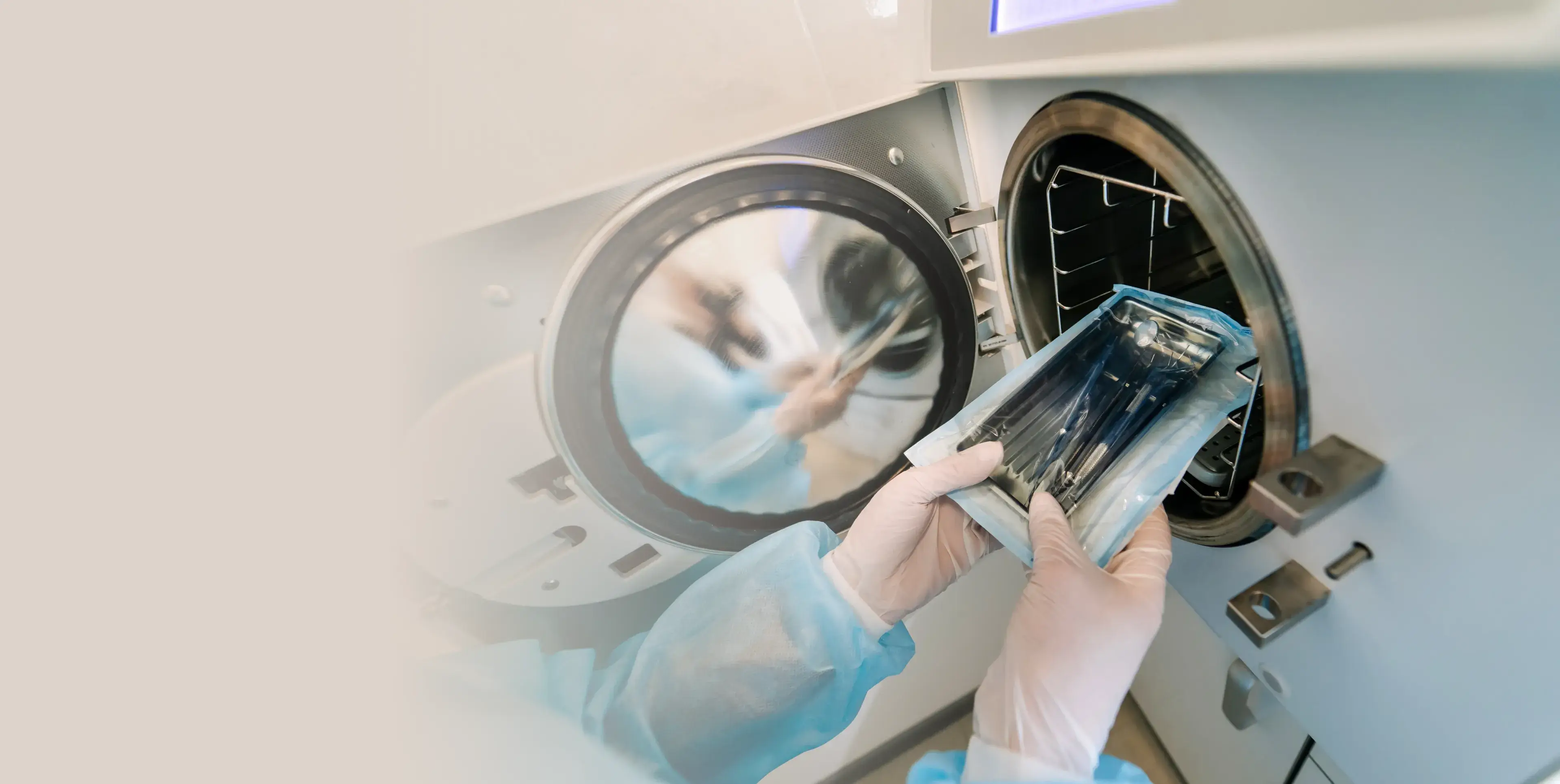 Healthcare professional in blue protective clothing placing sterilized medical instruments into an autoclave.