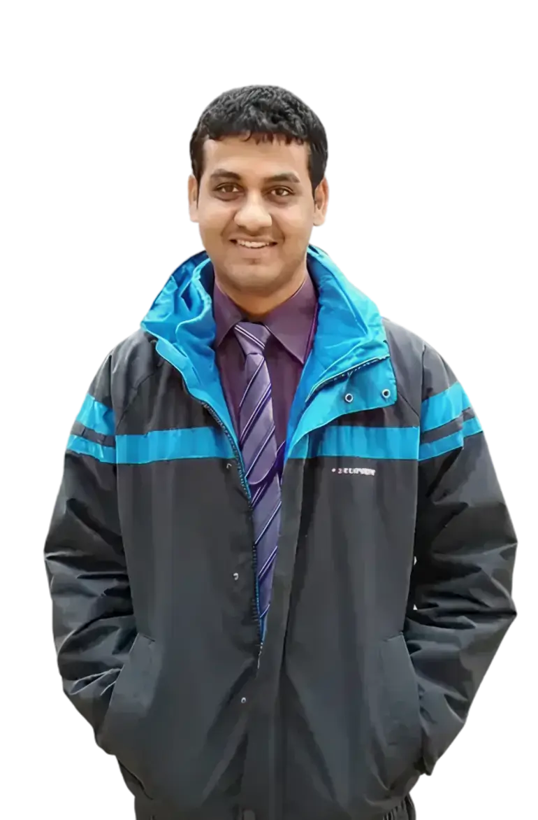 Smiling man wearing a black and blue jacket over a purple shirt and striped tie with hands in pockets.