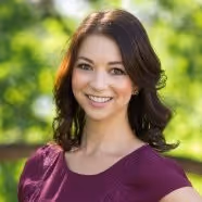Headshot of a woman in an outdoor setting, wearing a red top.