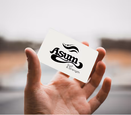 A hand holding a white business card with the logo for Asym Surf & Strength.